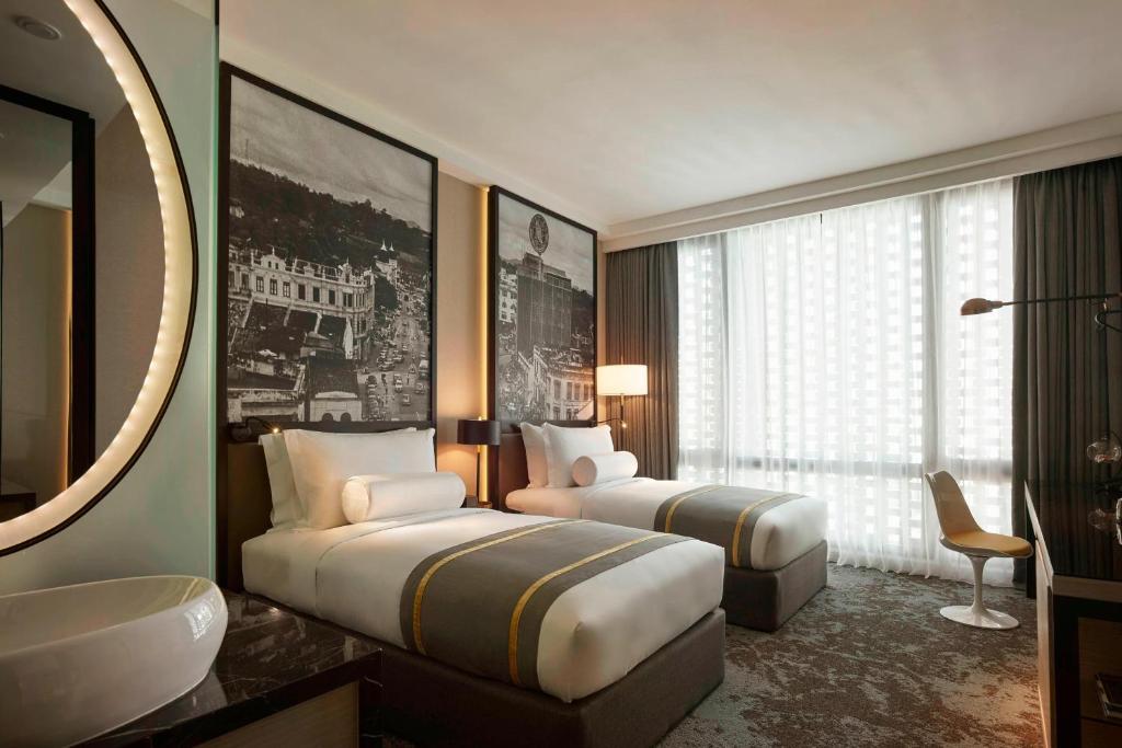 A twin room with matching beds, a large curtained window and a compact desk.