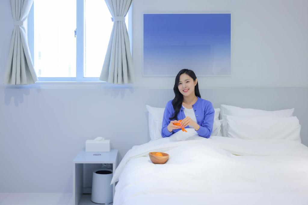 a woman sitting on top of a bed at Aank Air Hotel Chuncheon in Chuncheon