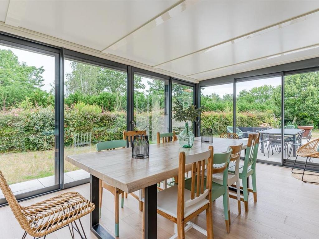 une salle à manger avec une table, des chaises et des fenêtres dans l'établissement Maison moderne près du lac avec jardin et véranda à Sanguinet, pour 10 personnes - FR-1-319-584, à Sanguinet