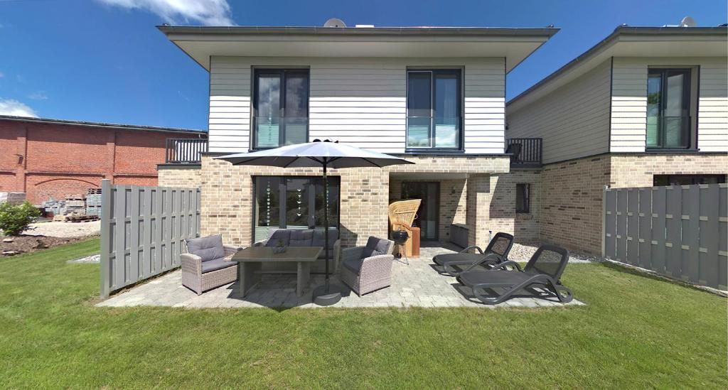 a patio with chairs and an umbrella in front of a house at Bauernhof Lafrenz Wellness - Ferienhaus Ostküste in Fehmarn