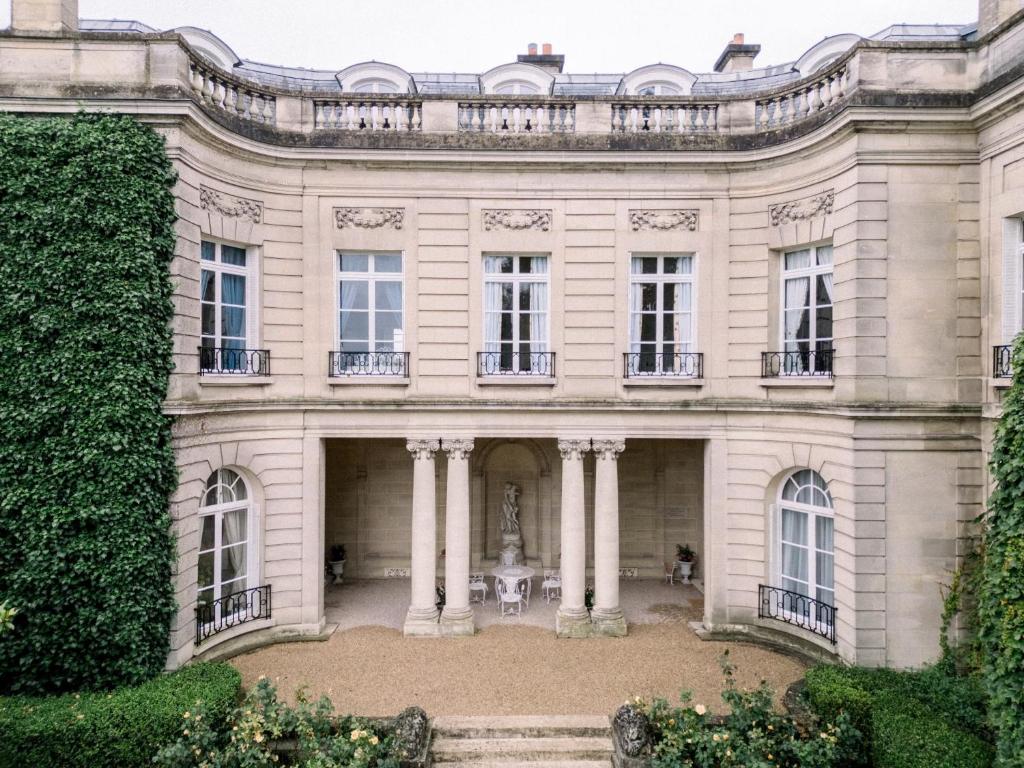 a large white house with columns and a statue at Château du Prieuré Évecquemont in Évecquemont