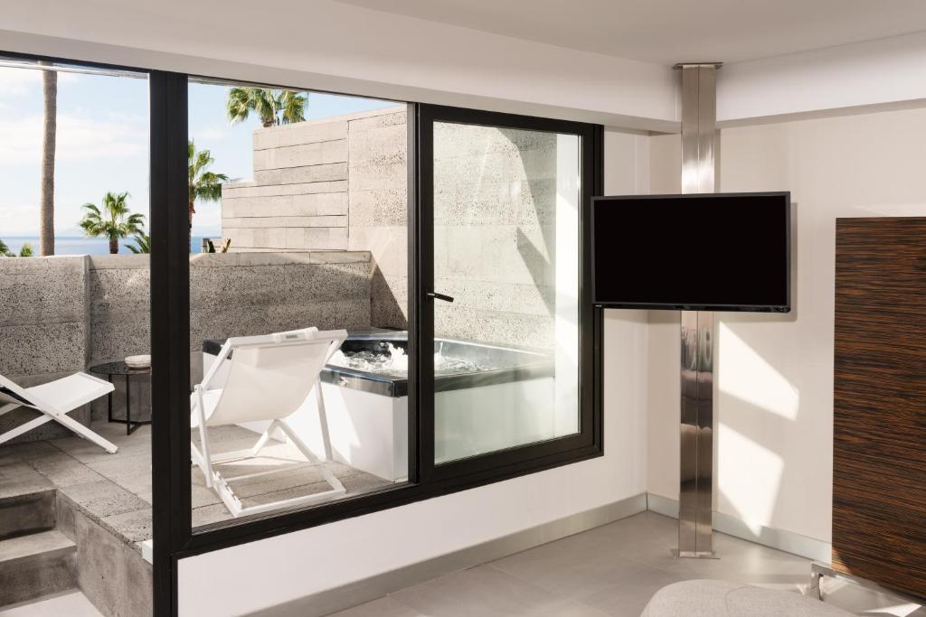 a living room with a large window with a chair and a television at La Isla y el Mar, Hotel Boutique in Puerto del Carmen