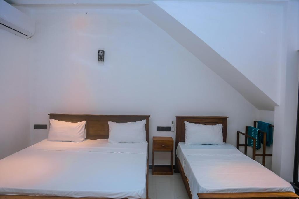 two beds in a room with white sheets at Mirissa Breeze in Mirissa