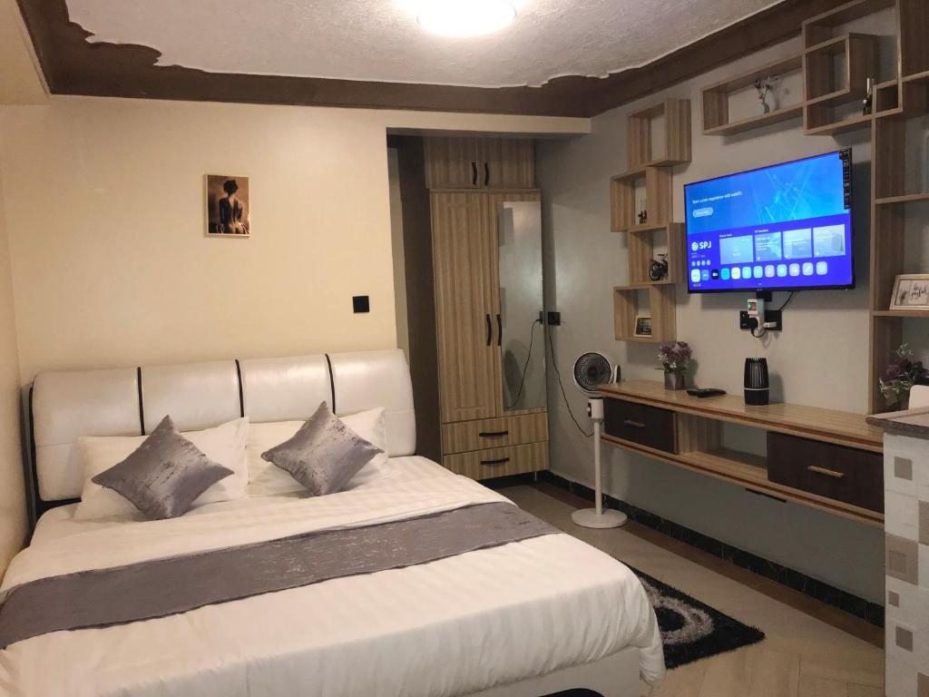 a bedroom with a white bed with a television on the wall at AG Home - Studio Kampala in Kampala