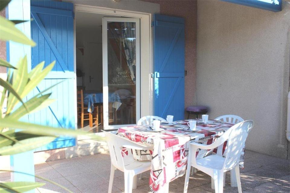 une table avec des chaises blanches et une porte bleue dans l'établissement Maison 3 pièces - Gruissan GA090-056, à Gruissan