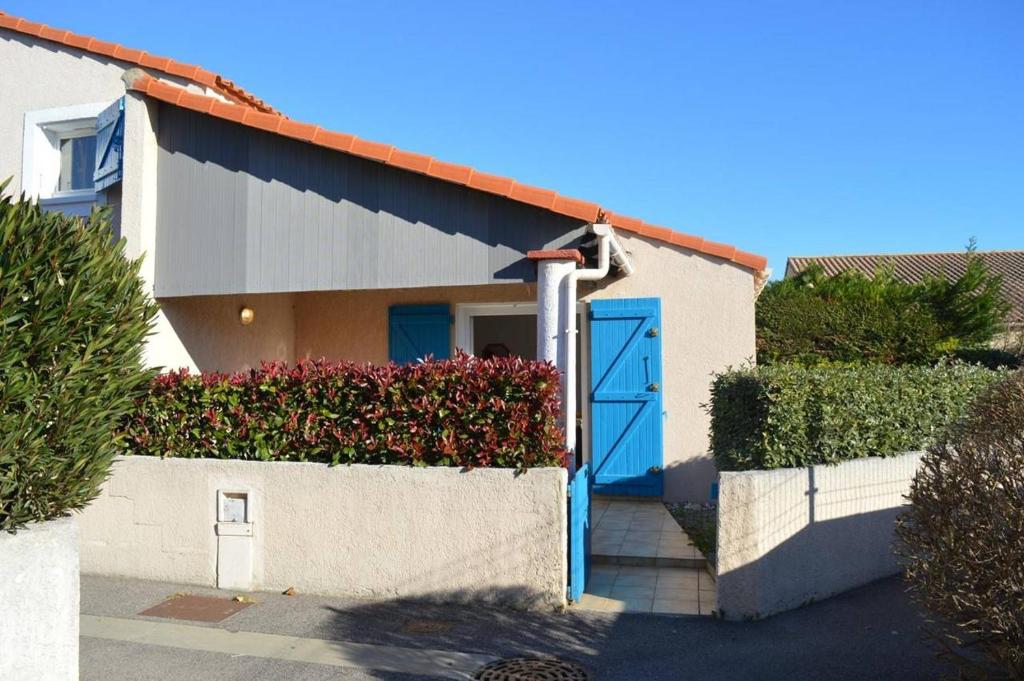 une maison avec une porte bleue et quelques buissons dans l'établissement Maison 2 pièces mezzanine 6 couchages SAINT CYPRIEN SC880-020, à Saint Cyprien Plage