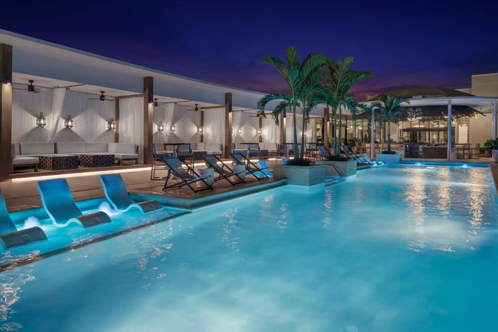 a swimming pool at night with blue chairs and palm trees at The Ben, Autograph Collection in West Palm Beach