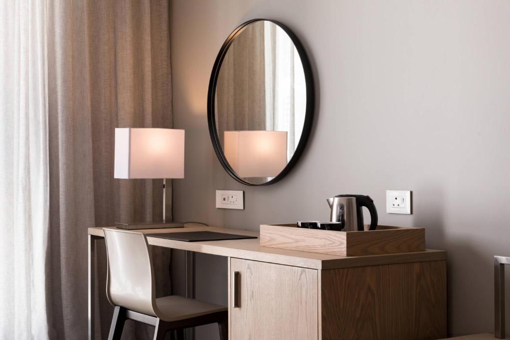 a vanity with a mirror and a table with a lamp at AC Hotel by Marriott Cape Town Waterfront in Cape Town