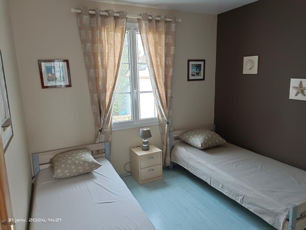 Dos camas individuales en una habitación con ventana. en maison île de Ré avec piscine chauffée et vélos, en Le Bois-Plage-en-Ré