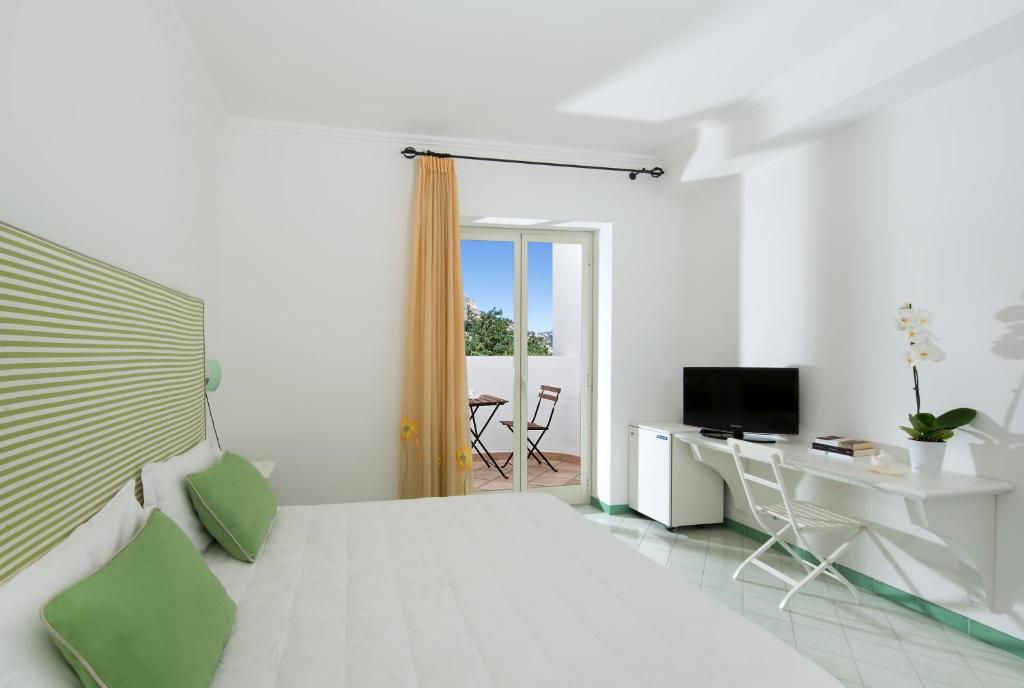 a white bedroom with a bed and a desk and a television at Hotel Le Terrazze in Conca dei Marini