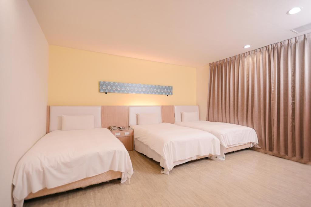 two beds in a room with white sheets at i-Deal Hotel in Taichung
