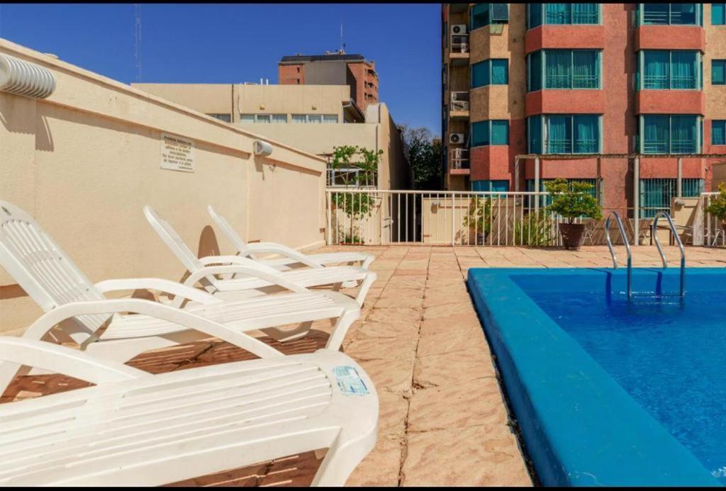 einen Pool mit weißen Stühlen neben einem Gebäude in der Unterkunft MZA Departamentos in Mendoza