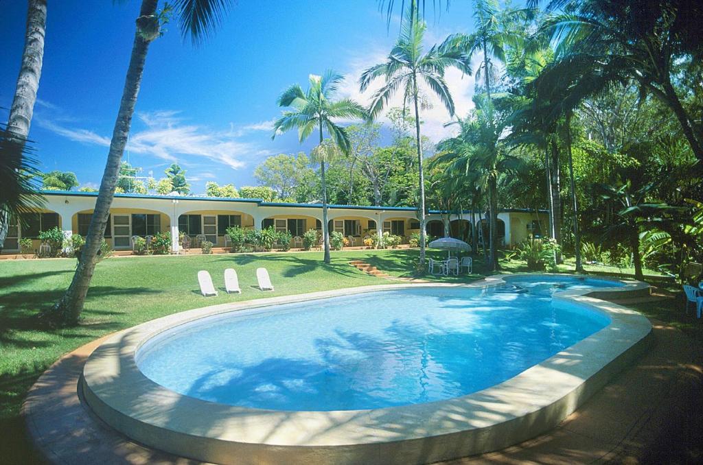a swimming pool in front of a house with palm trees at Villa Marine Holiday Apartments Cairns in Yorkeys Knob
