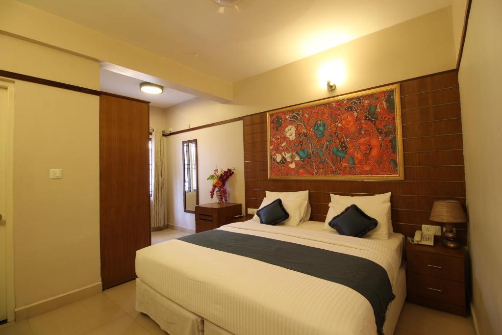 a bedroom with a large bed and a painting on the wall at Srivar Hotels in Guruvāyūr