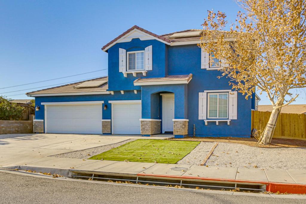 a blue house with two white garage doors at Pool Table and Charcoal Grill Home in Victorville! in Victorville