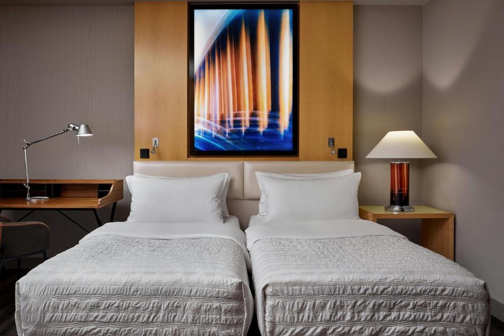 two beds in a hotel room with a painting on the wall at Le Méridien Munich in Munich