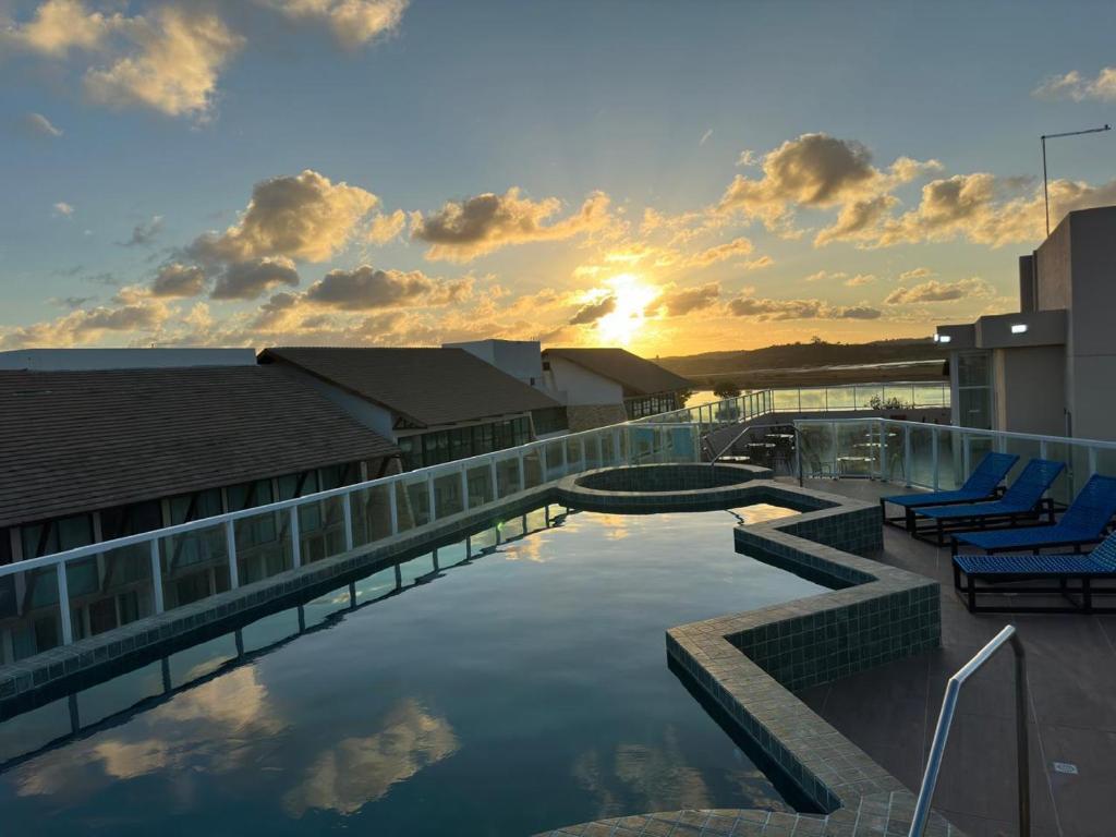 ein Gebäude mit einem Pool mit Stühlen und dem Sonnenuntergang in der Unterkunft Eco Miragem Residence - Porto de Galinhas in Porto De Galinhas