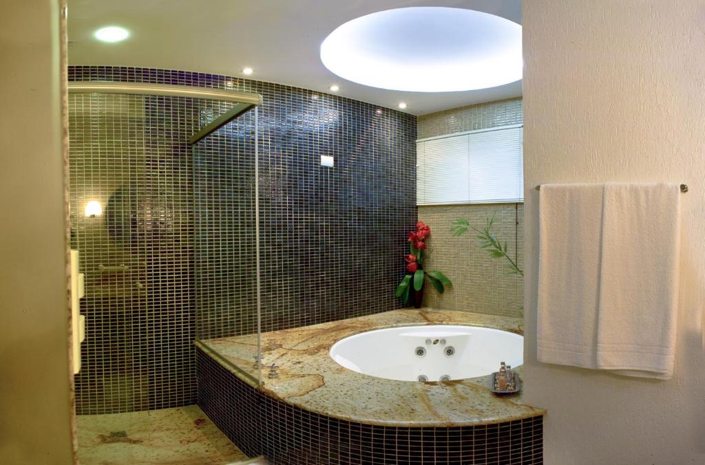 a bathroom with a tub and a glass shower at Benvenuto Palace Hotel in Governador Valadares