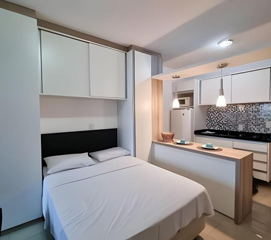Un dormitorio con una cama blanca y una cocina. en Prédio Central, en Curitiba