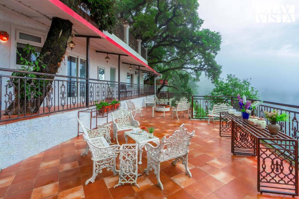 Un patio con mesas y sillas en un balcón. en StayVista at Aspen Heights Hidden In Clouds, en Mussoorie