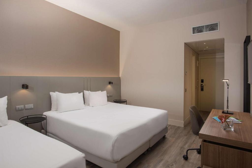 a hotel room with two beds and a desk at NH Trieste in Trieste