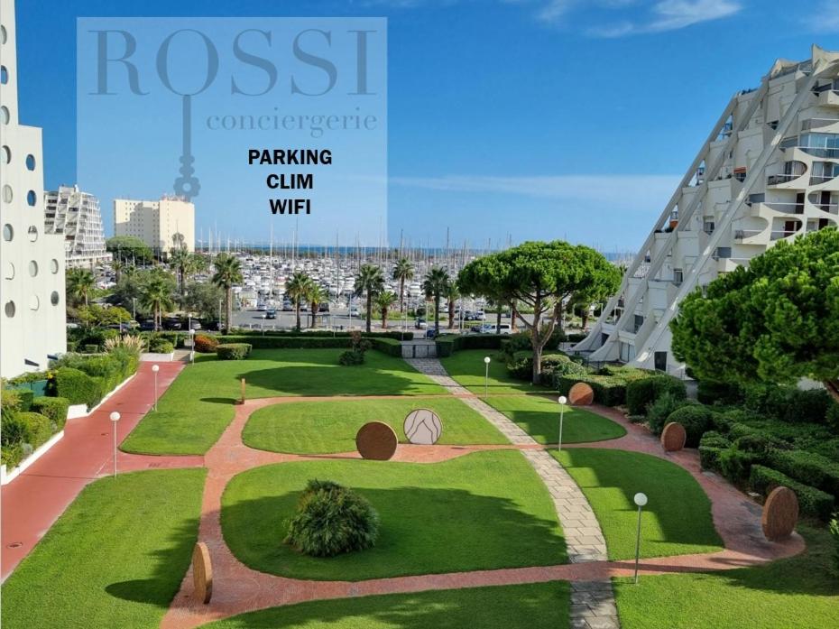 - une vue sur un parc avec un bâtiment en arrière-plan dans l'établissement T2 FIDJI vue Port et Mer Parking CLIM Wifi - ROSSIconciergerie - Linge en option, à La Grande Motte