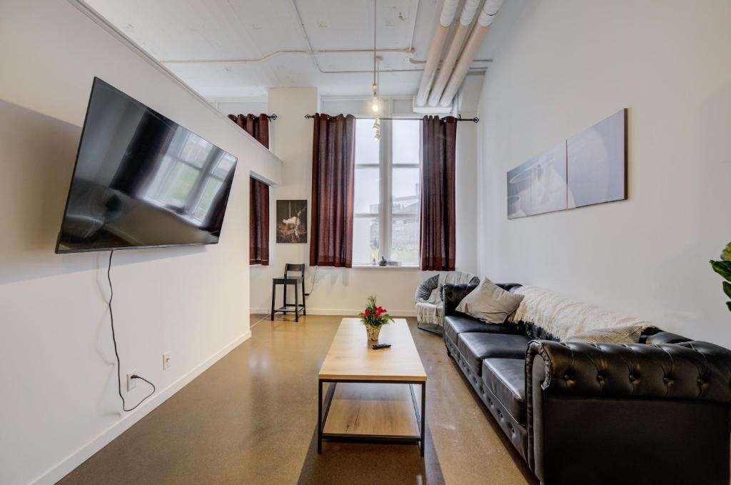 a living room with a black leather couch and a tv at Entire 1 bedroom in the heart of KW downtown across Google in Kitchener