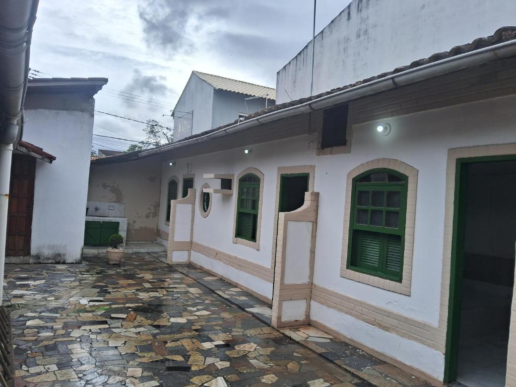 a white house with green doors and a stone courtyard at Pousada Familia in Rio das Ostras