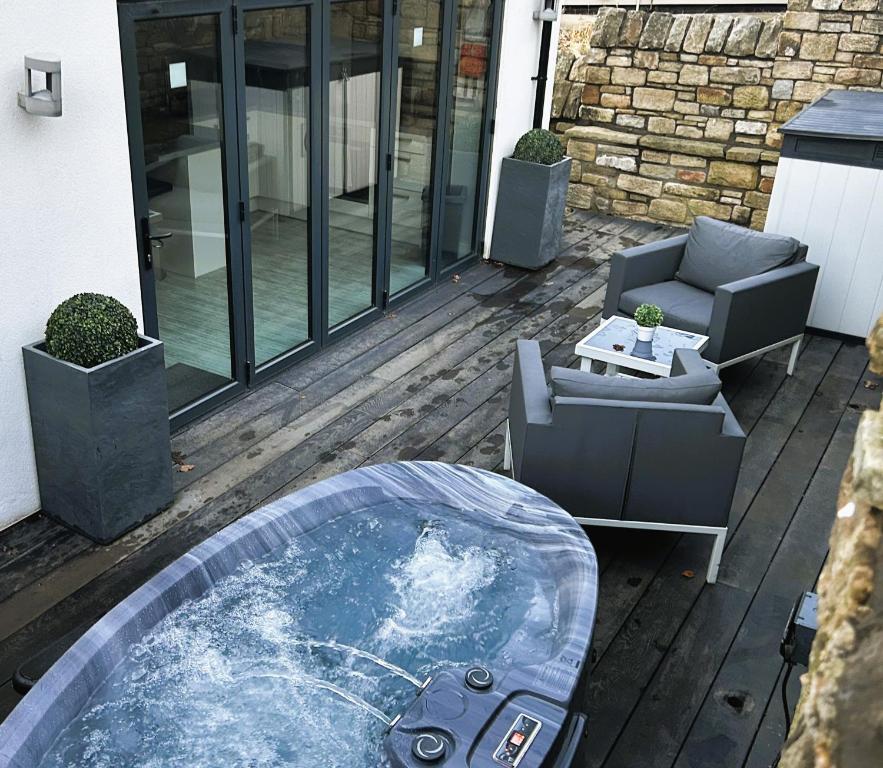 a hot tub on a deck with a couch and a chair at Couples Canalside Retreat with Hot Tub & Pergola in Poynton