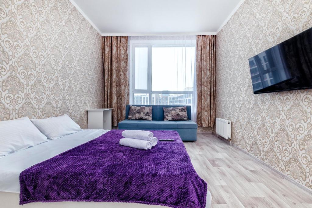ein Schlafzimmer mit einem lila Bett und einem blauen Sofa in der Unterkunft Уютная квартира на левом берегу in Astana