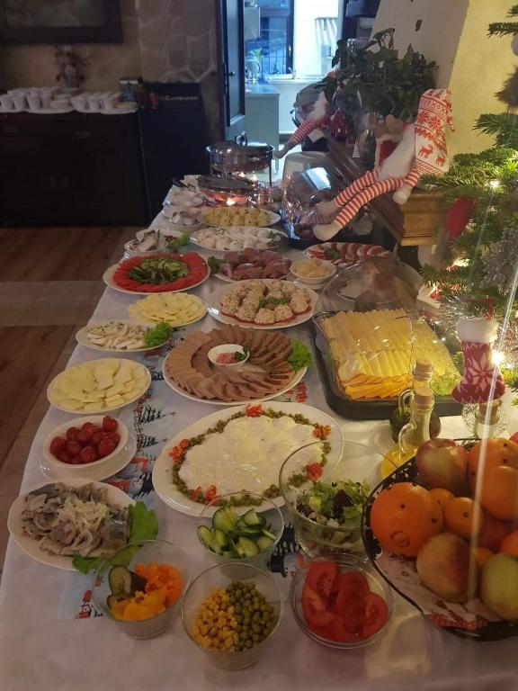 Long indoor buffet table filled with salads, cheeses, cold cuts, bowls of fruit and festive decorations.