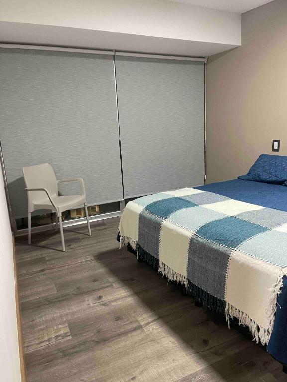 a bedroom with a bed and a chair and a window at Calido departamento Parque in Villa Marini