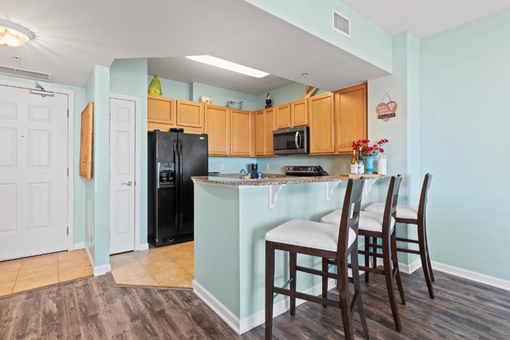 a kitchen with a bar with chairs and a refrigerator at 5 Star Resort 11th Fl Stunning Sunrise 2BR 2BA King Suite,Pools ,Shuttle or Walk to Beach in Destin