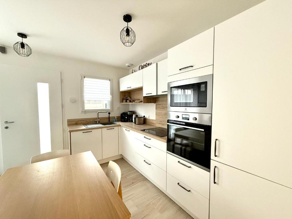a kitchen with white cabinets and a wooden table at Maison à 100m de la mer in Hermanville-sur-Mer