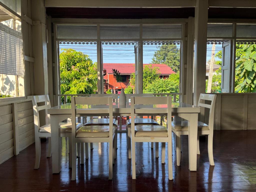 a white dining room table with white chairs and windows at Once in Lampang Guesthouse in Lampang
