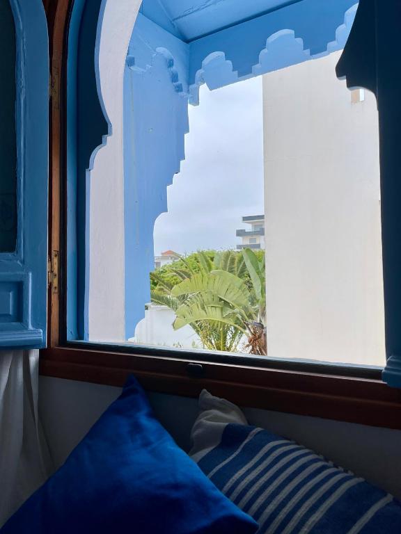 a window with a view of a palm tree at Hotel Al Alba Hammam & Restaurant in Asilah