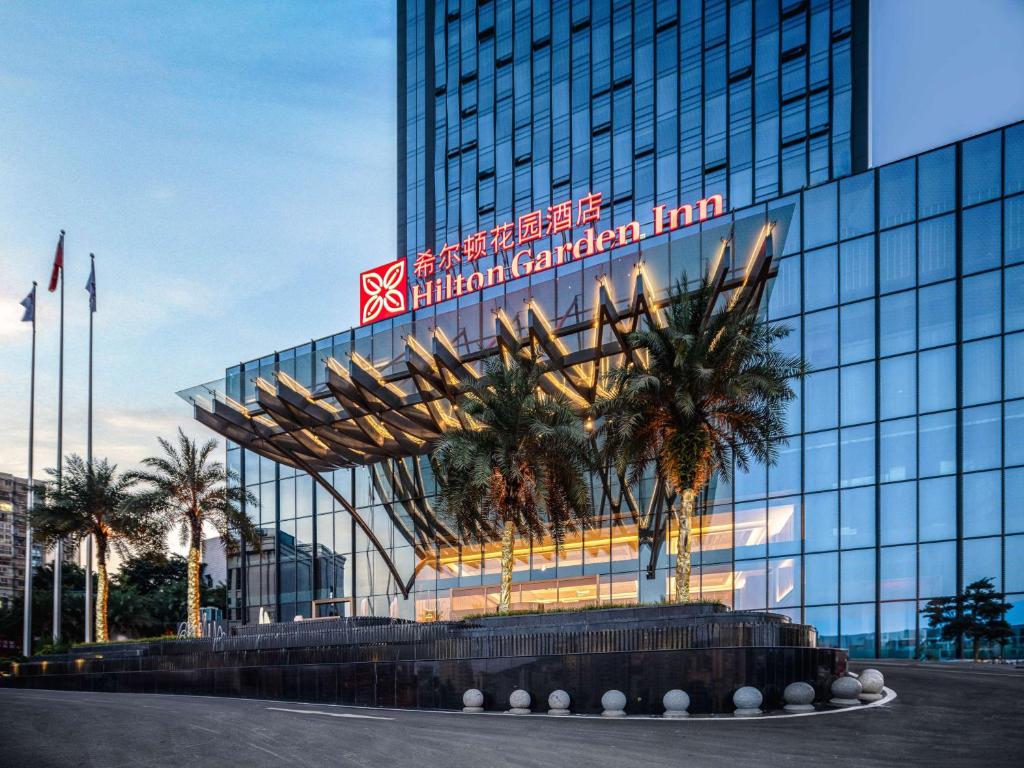 巴中巴中巴州希尔顿花园酒店的一座大型玻璃建筑,前面有棕榈树