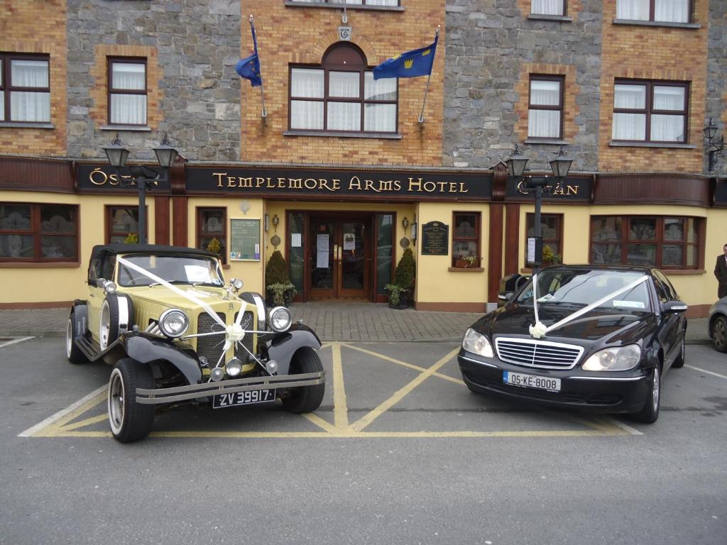 dos autos estacionados en un estacionamiento frente a un edificio en Templemore Arms Hotel, en Templemore