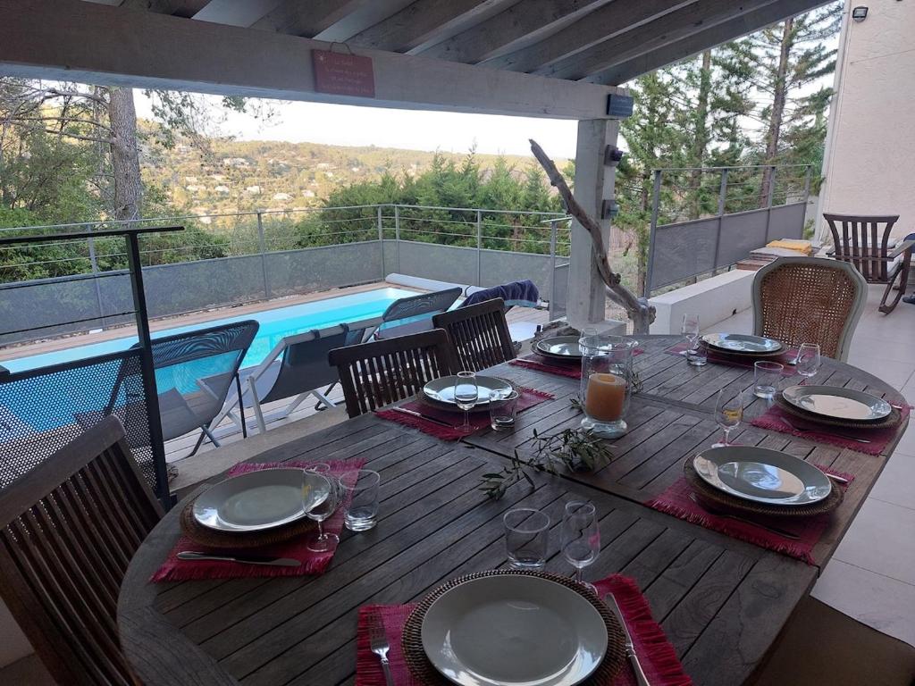 - une table en bois avec des assiettes et des verres à vin à côté de la piscine dans l'établissement Cinette - Climatisation & Piscine chauffée, à Cotignac