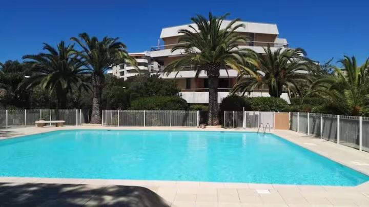 une grande piscine avec des palmiers et un bâtiment dans l'établissement Fréjus, 200 m des plages appart f1 avec piscine, à Fréjus