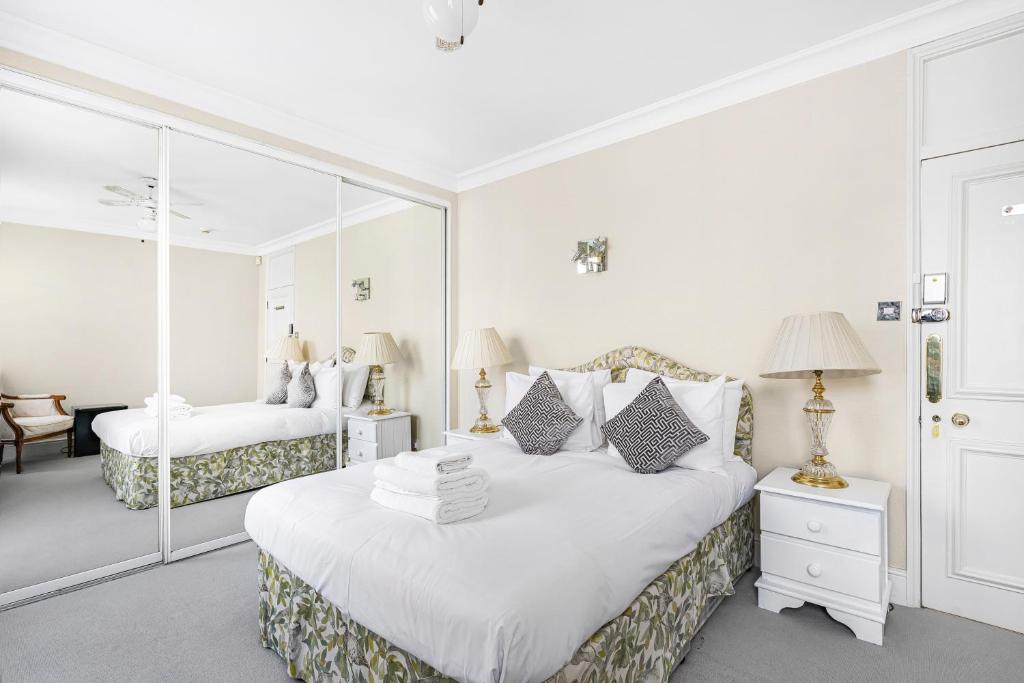 a white bedroom with two beds and a mirror at Hyde Park Rooms in London