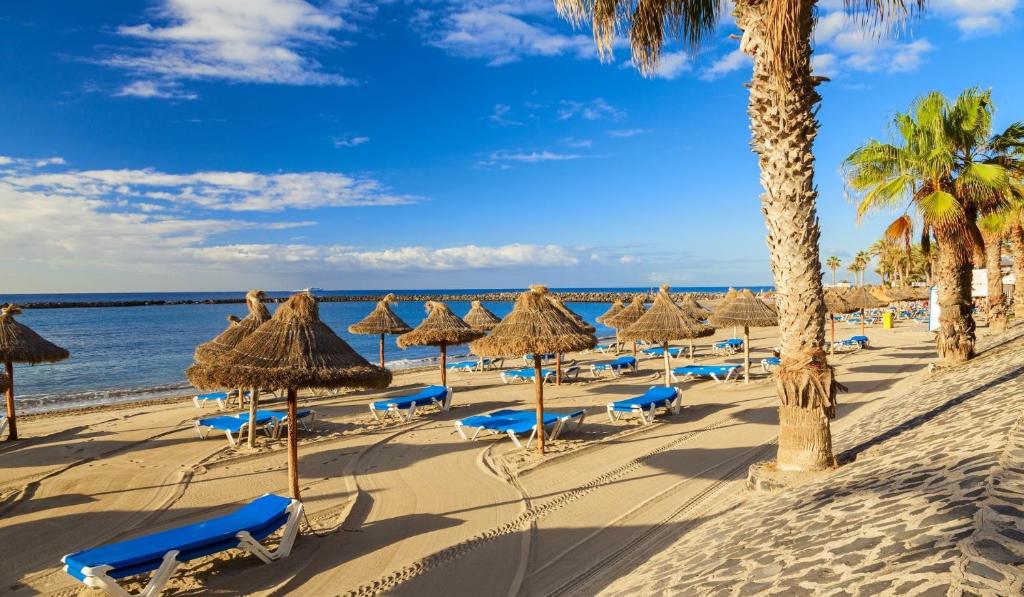 una playa con sombrillas y sillas de paja y el océano en Casa Valdes Los Cristianos Center, en Los Cristianos