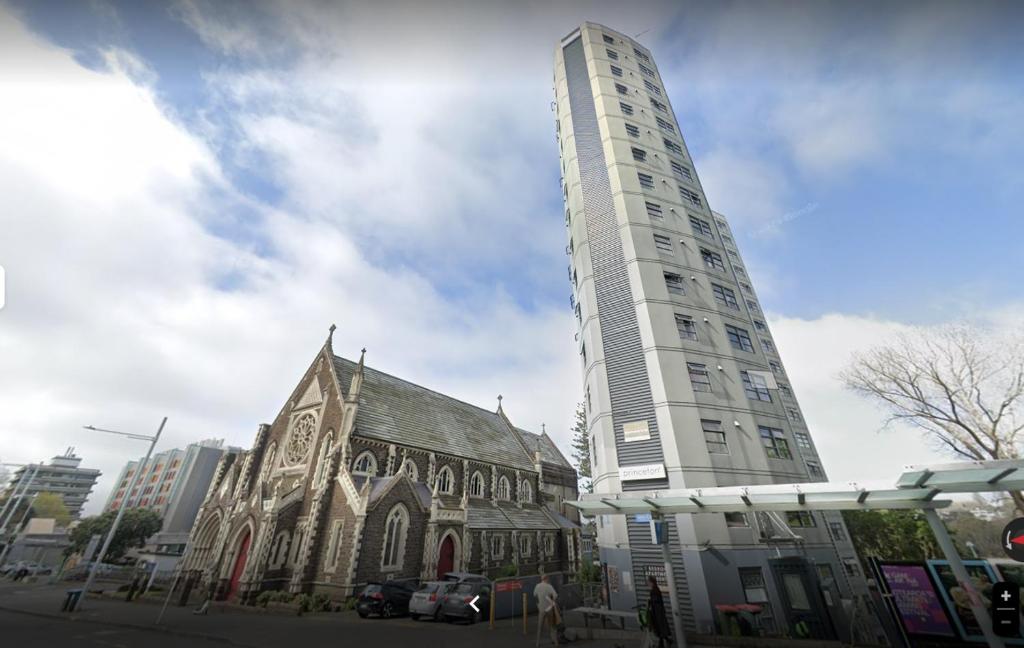 a tall white building next to a church at Princeton 30 Symonds Street in Auckland