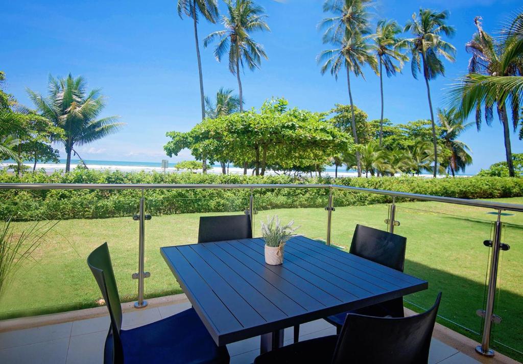 a blue table and chairs on a balcony with palm trees at Oceanfront Balcony Condo 2101 | Playa Bejuco + Sunset Views + Pool in Esterillos