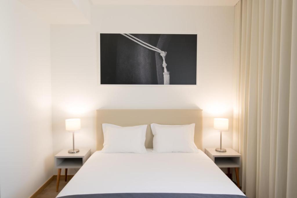 ポルトにあるポルト コロシアム ホテルのベッドルーム(白い大型ベッド、ランプ2つ付)
