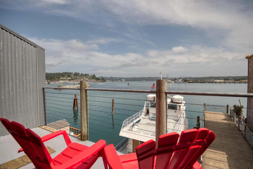 a deck with red chairs and a boat on the water at Captains Quarters - Anchor Pier Lodge in Newport