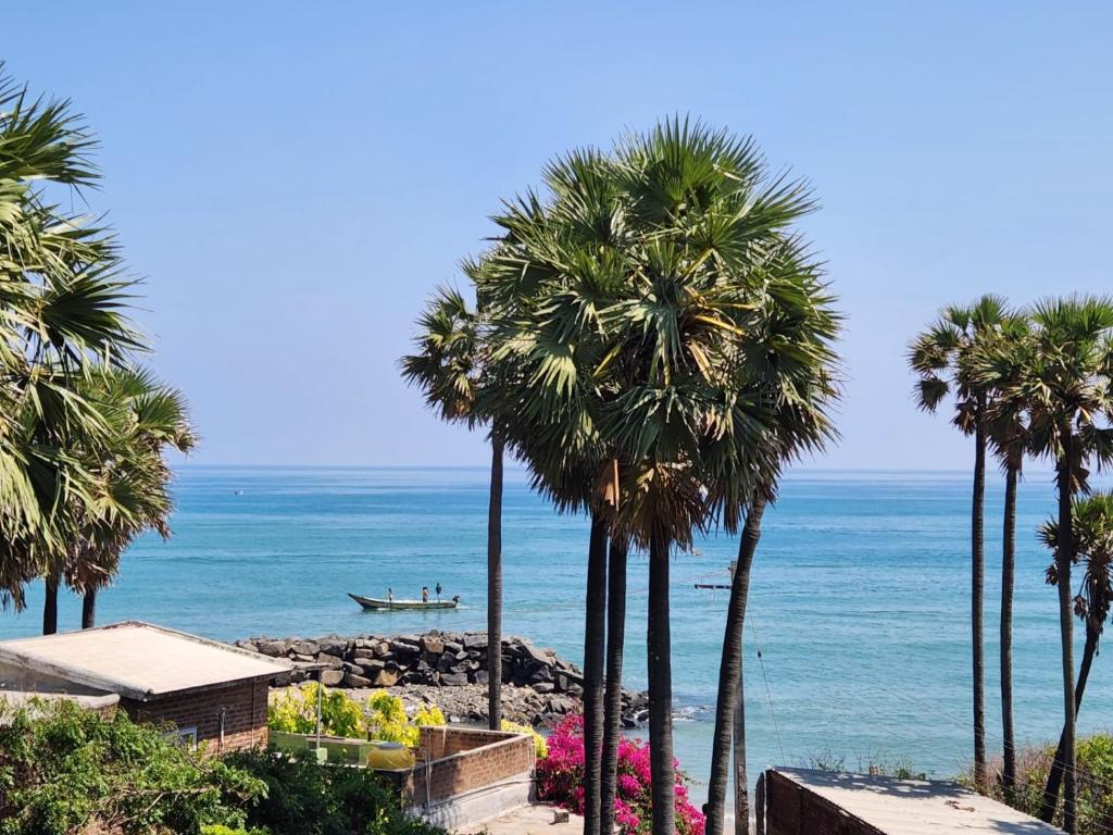 a beach with palm trees and a boat in the water at Angel Beach Villas - Pondicherry in Puducherry