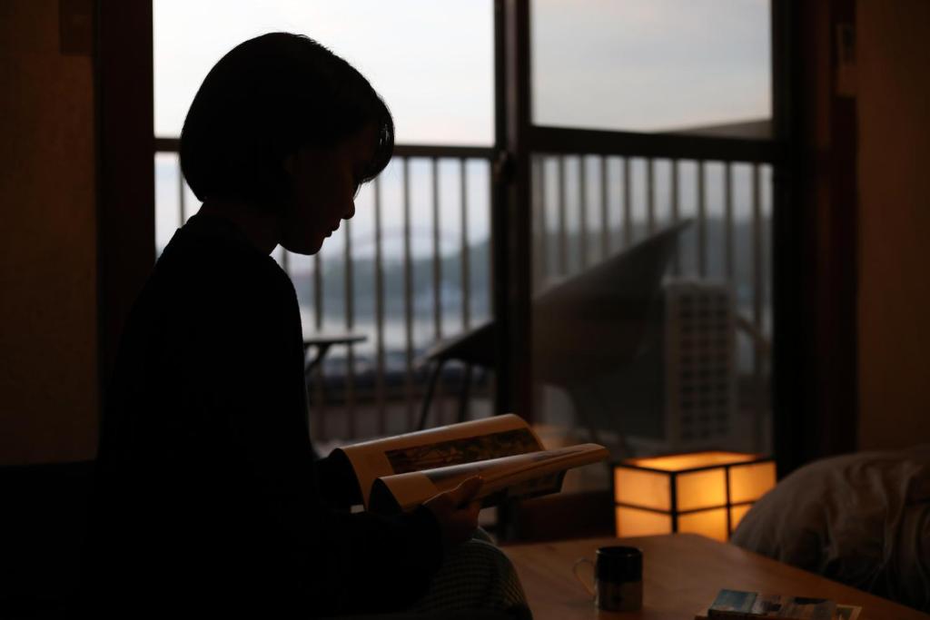 a boy reading a book in front of a window at Guesthouse SETOUCHI LIFE in Kure
