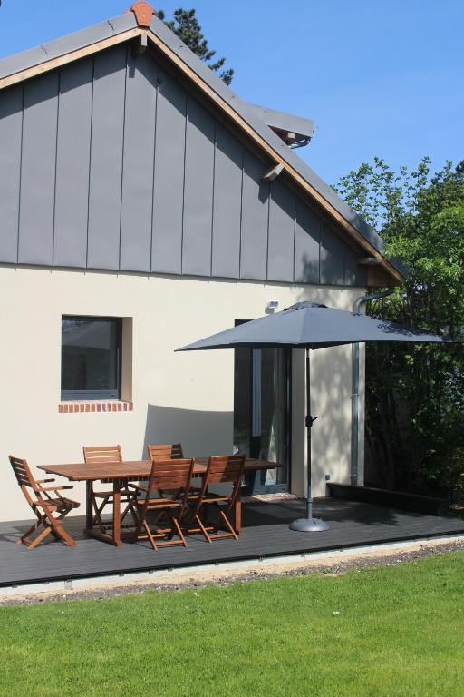 un patio avec une table, des chaises et un parasol dans l'établissement L'idylle - maison a la mer, à Quiberville
