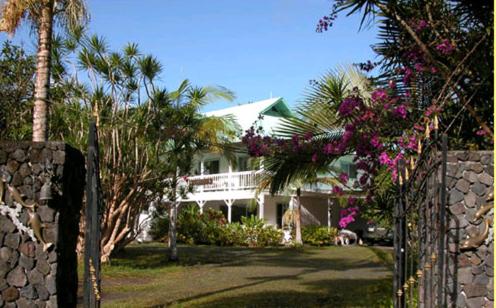 a white house with palm trees and a fence at Lava Tree Tropic Inn in Pahoa